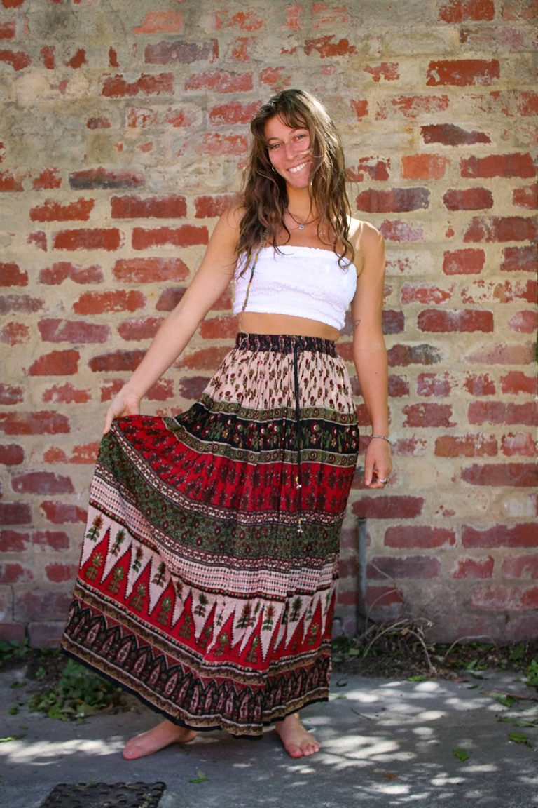 Woman in a white top and block-print crinkle skirt by a brick wall