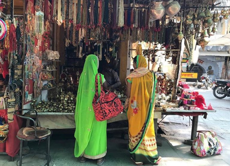 Women in emerald and marigold saris browsing a jewellery stall