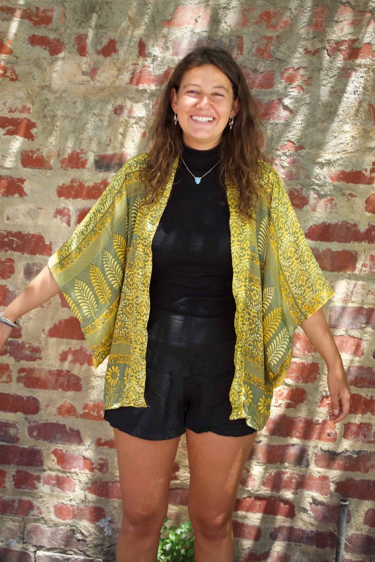 Smiling woman wearing a gold sari-silk kimono against a brick wall