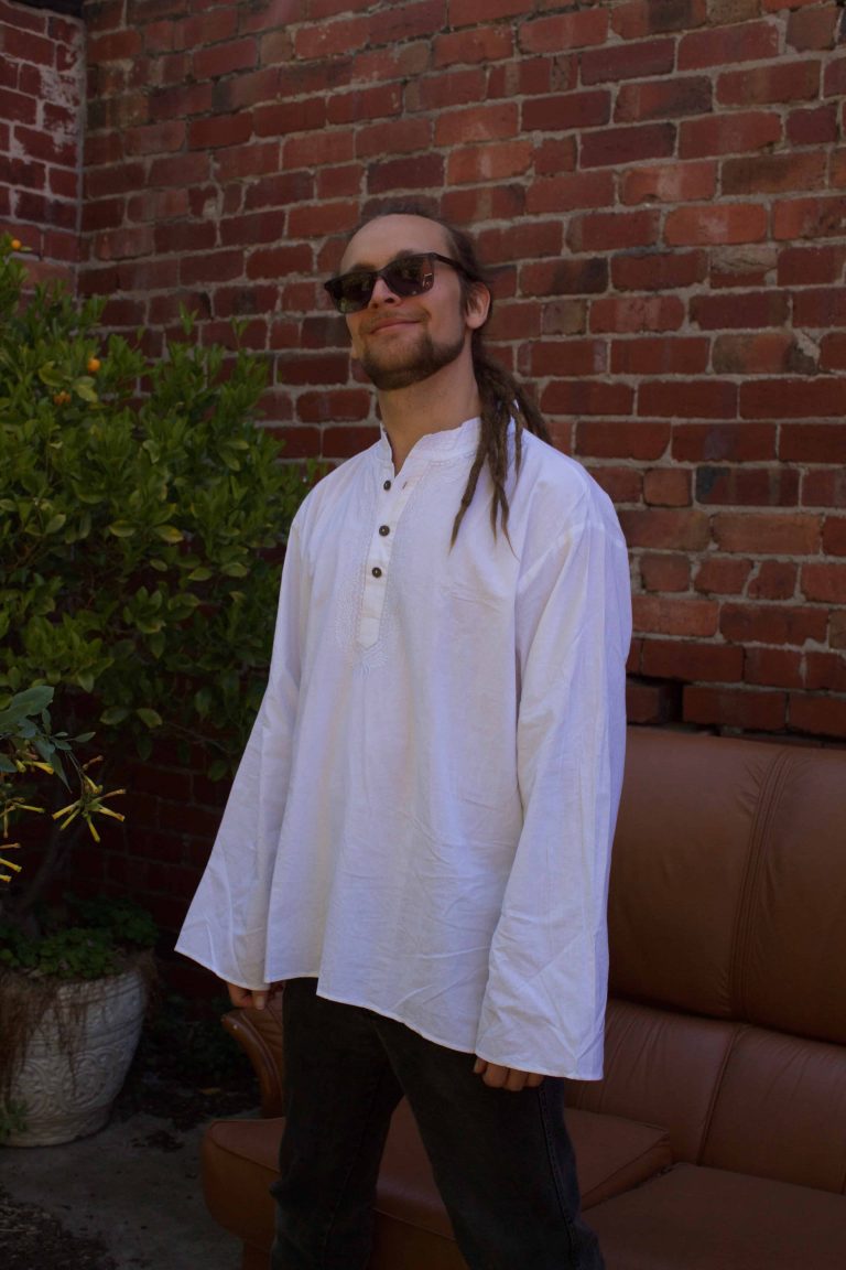 Man in a collarless white cotton shirt beside a red-brick wall