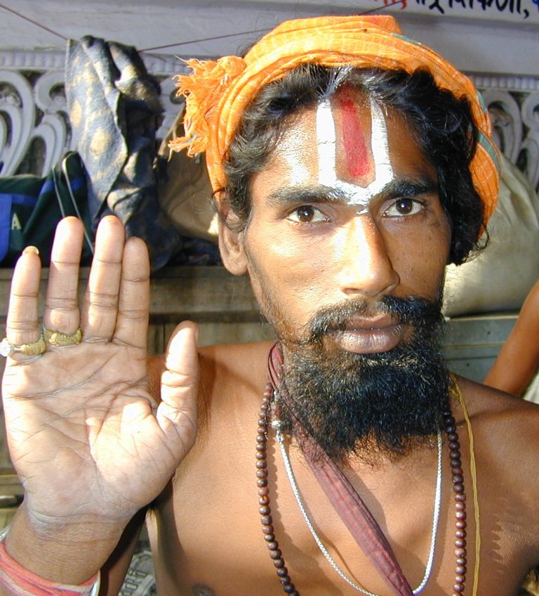 Young sadhu with painted brow raising a palm in greeting