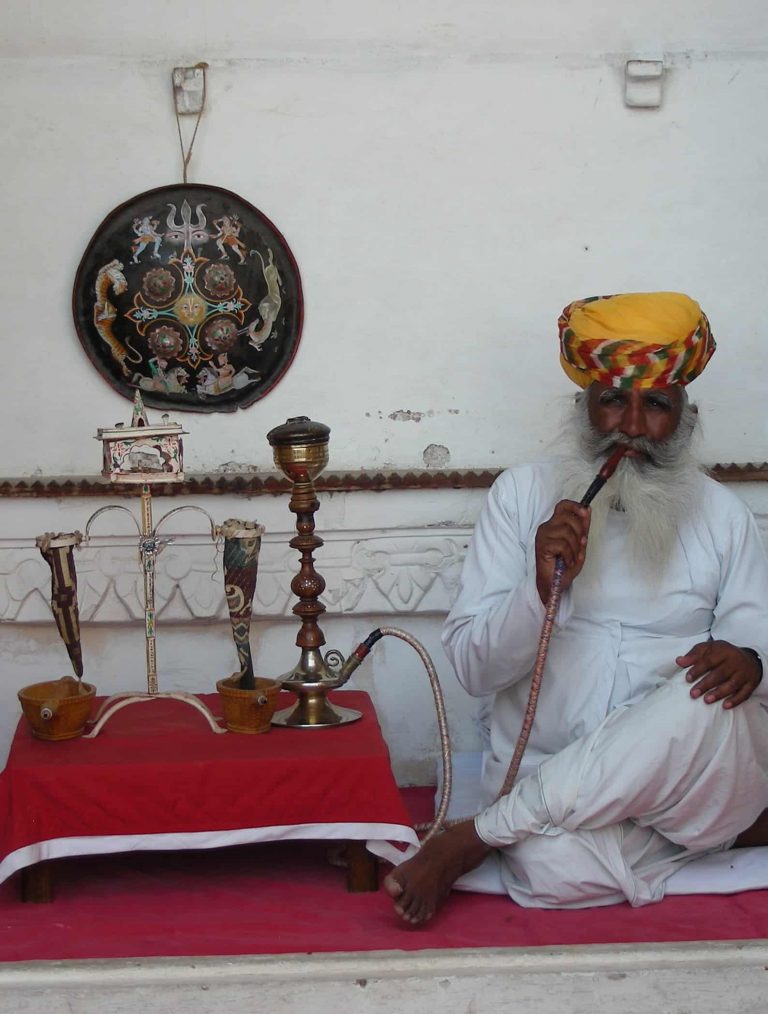 Elder in a saffron turban drawing on a hookah beside brass wares