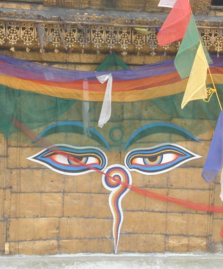 Painted eyes of a Nepali stupa beneath strings of prayer flags