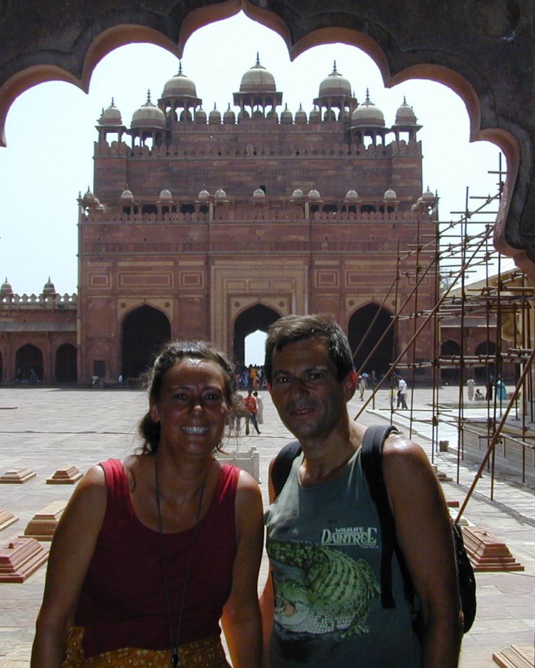 Two travellers smiling before a towering sandstone gateway