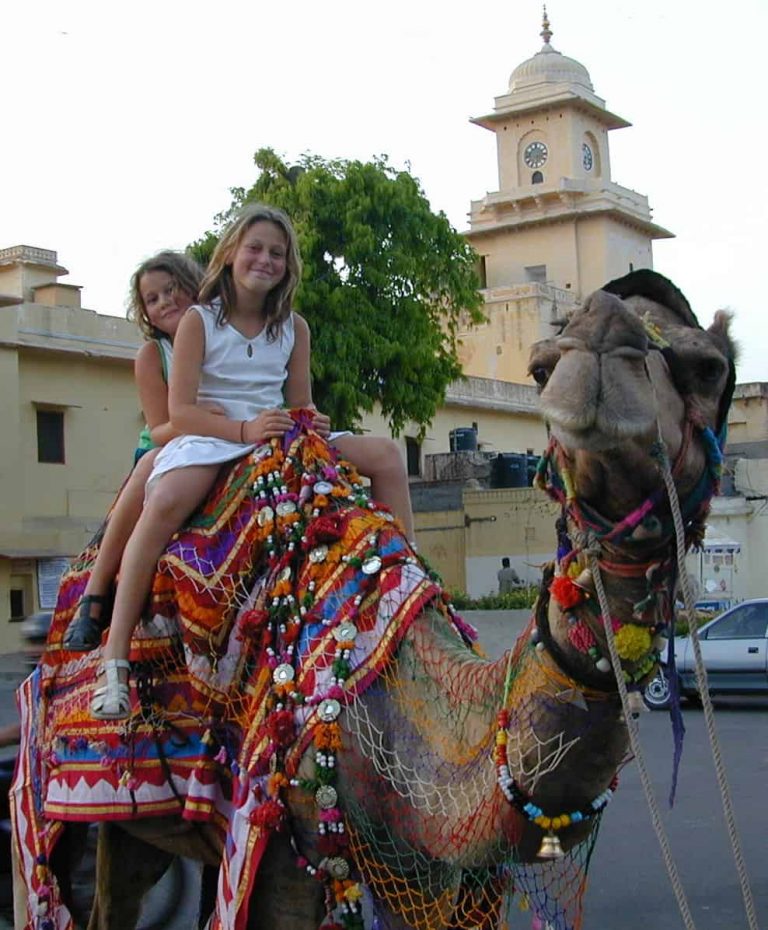 Children riding a mirrored, tasselled camel through a palace square