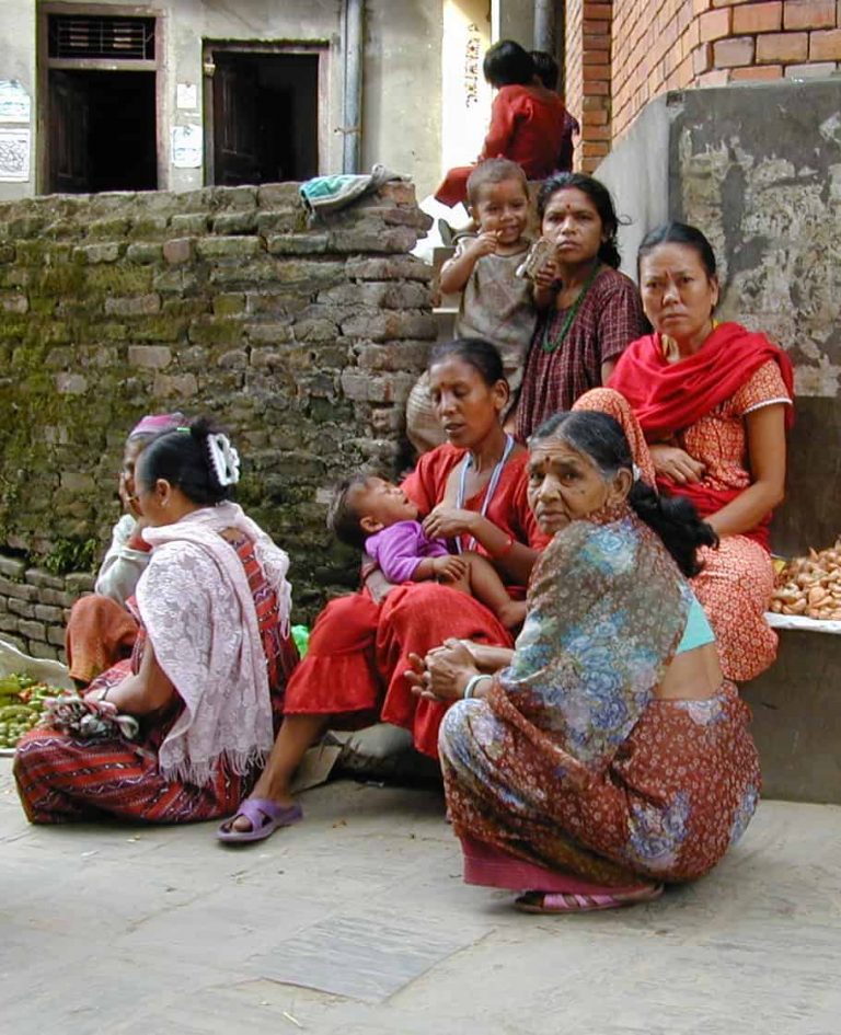 Mothers and babies resting against a stone wall at the market