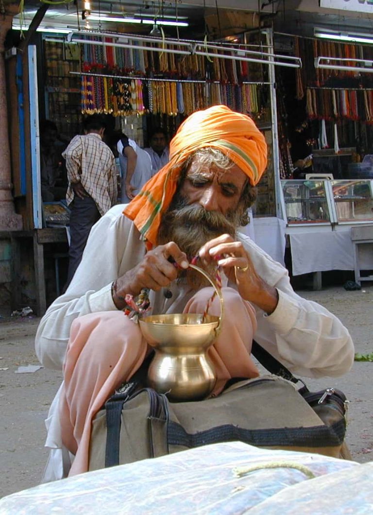 Turbaned craftsman working over a brass pot at his stall