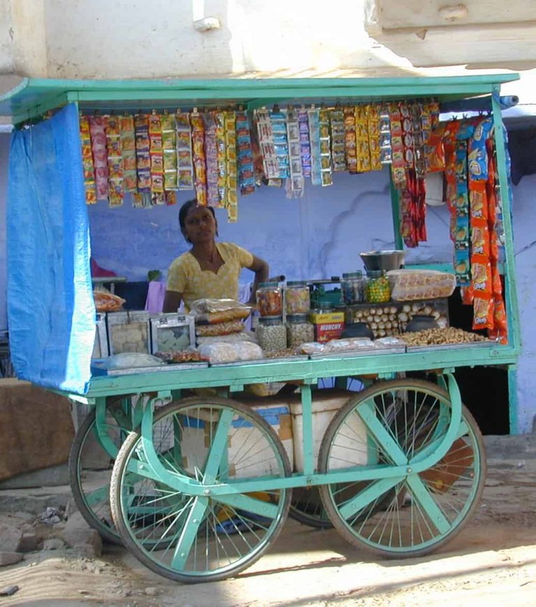 Snack vendor at his turquoise cart hung with foil packets