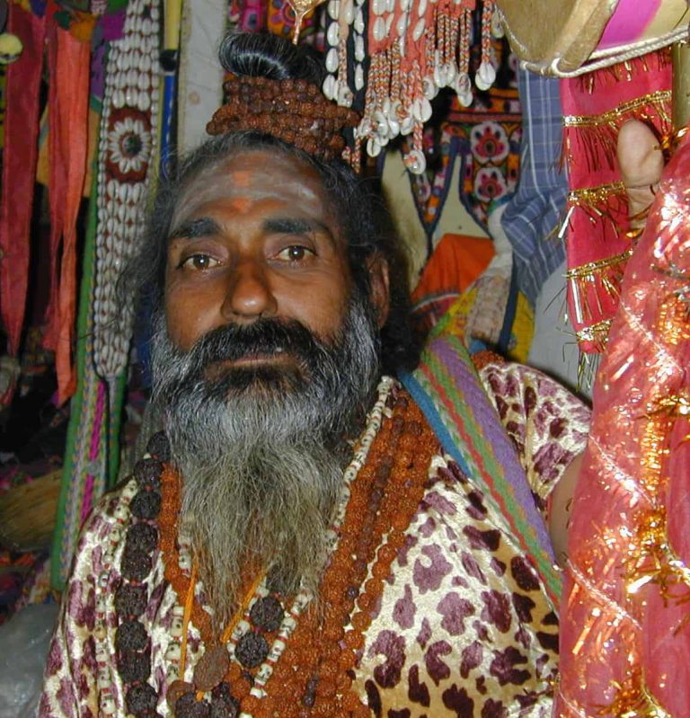 Bearded sadhu seated among the garlands of a market stall