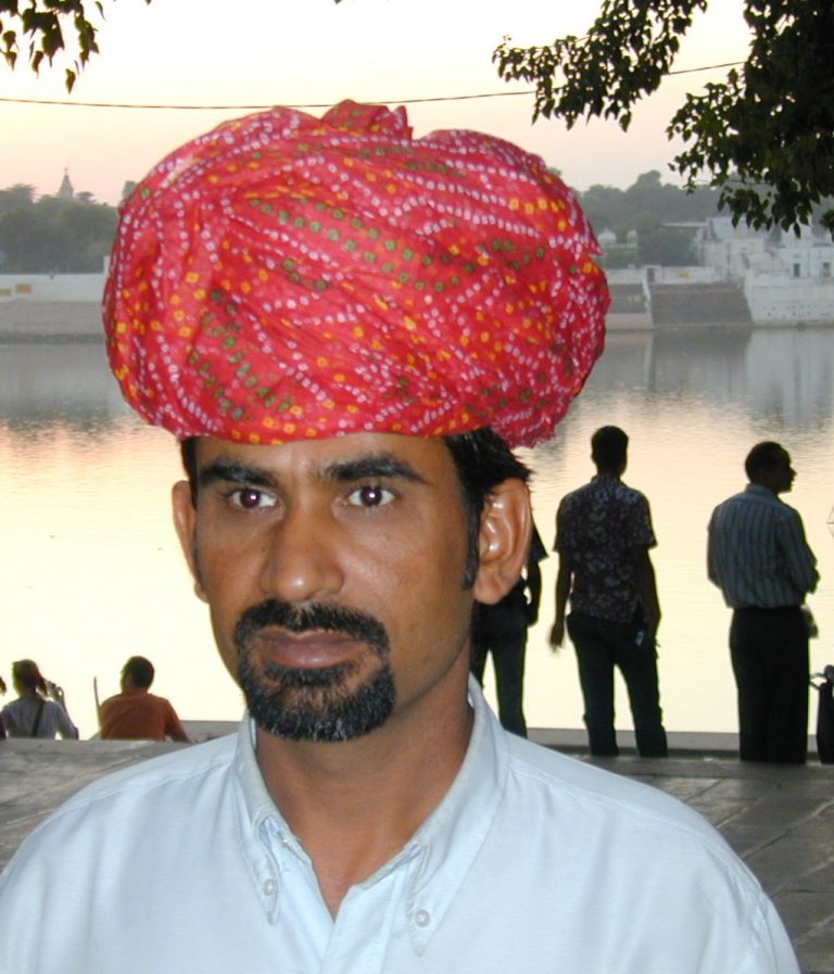 Man in a red bandhani turban at the lakeside ghats at dusk